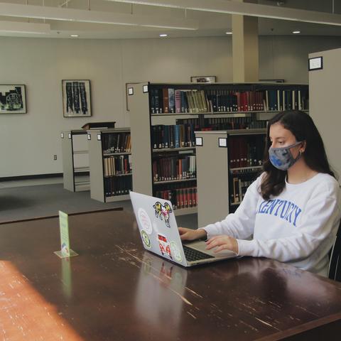 photo of masked student working on laptop in library