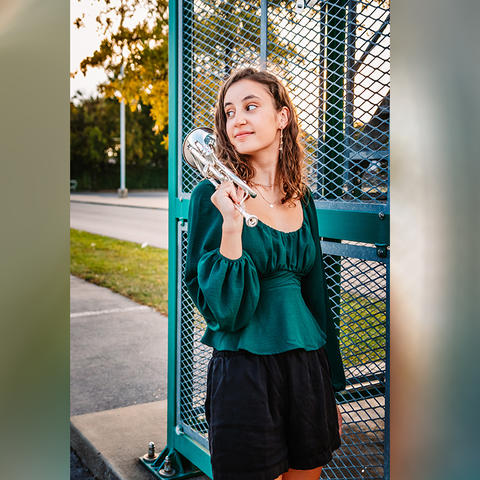 Woman in a green top outside, next to a metal structure, holding a trumpet. 