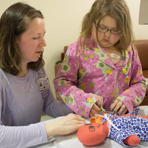 Child Life Specialist Ashley Rapske helps young Shannon understand how IVs work by practicing on a doll.