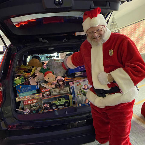 photo of UK Police Chief Joe Monroe dressed as Santa Claus in December 2019. He is standing by a vehcile packed with donated toys.