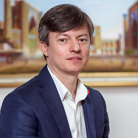 Professional head-and-shoulders portrait of a person wearing a navy blue blazer and white collared shirt.