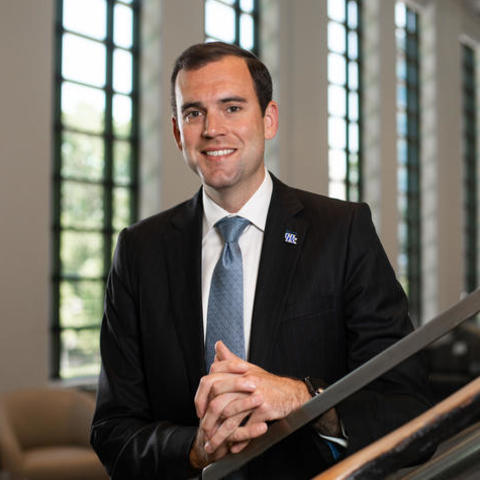 Eric King wears a suit and poses for a photo along a railing in the Gatton Student Center
