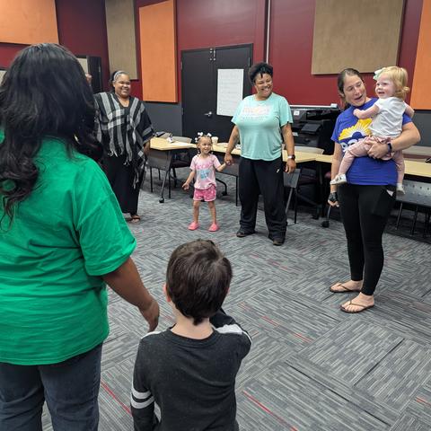 Parents standing around in a circle with three children. One person is holding a baby and the other two children are standing next to adults. 