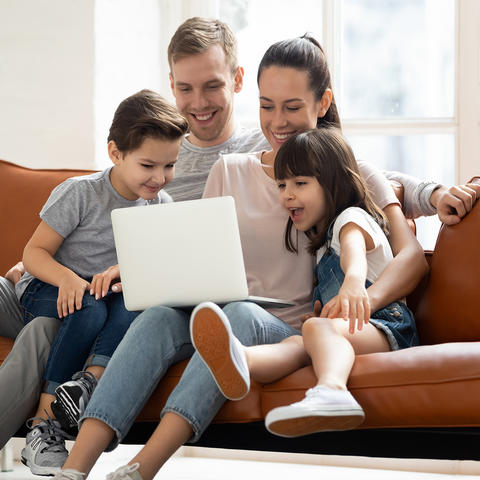 family sitting on sofa looking at laptop computer