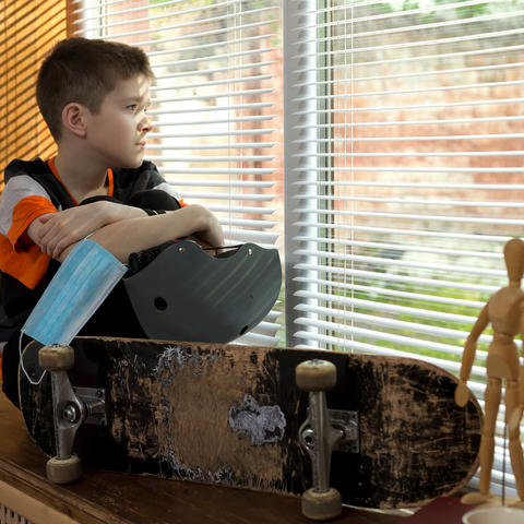 stock photo of boy sitting in windowsill with skateboard, helmet and mask in hand