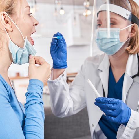 stock photo of health care professional in mask and shield swabbing young adult's mouth