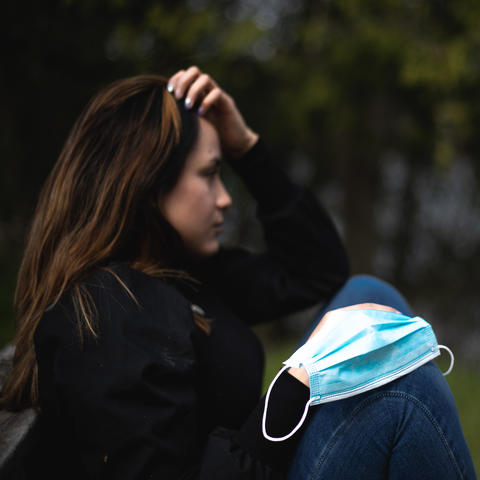 photo of young woman outside coping with stress of social isolation, face mask on knee