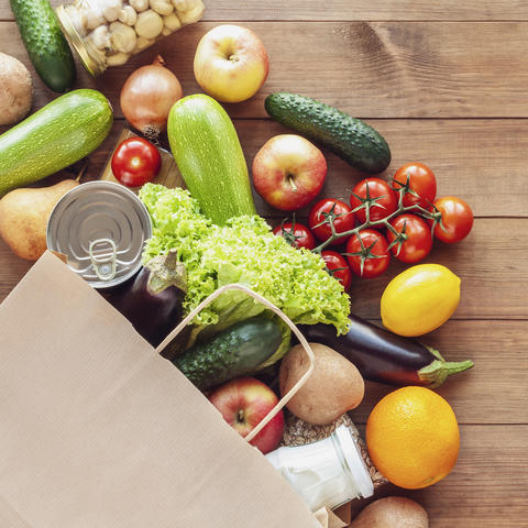 Paper grocery bag with fresh vegetables, fruits, milk and canned goods on wooden backdrop