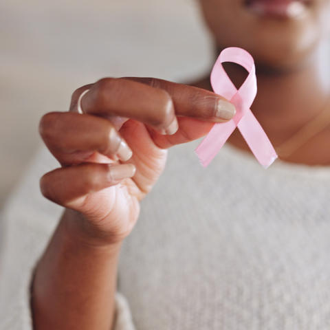Close-up of a person holding a pink ribbon in front of a white shirt.