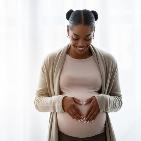 Image of Black woman holding her belly and smiling