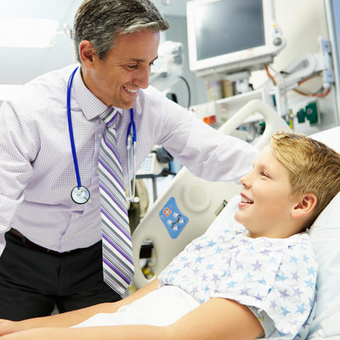 image of doctor leaning talking to boy in hospital bed