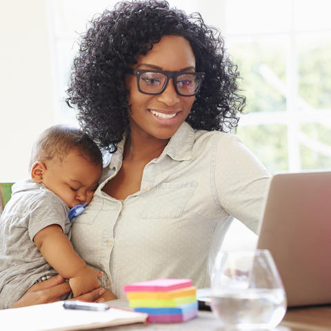 photo of woman working from home while holding a baby