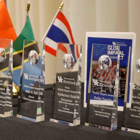University of Kentucky 2025 Global Impact Award trophies displayed on a table with international flags behind them.
