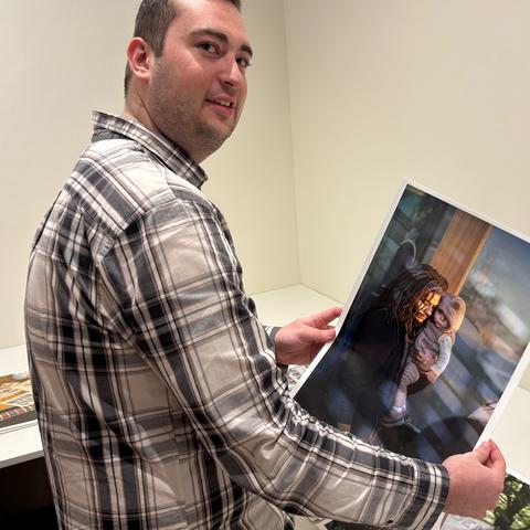 white male wearing a plaid shirt, holding a photo print, standing in a gallery with white walls