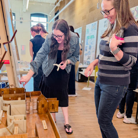Two people smile as one points to a detailed architectural model at an exhibition.
