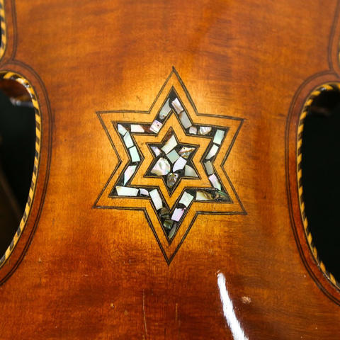 A close-up of the back of a violin featuring an inlaid six-pointed star design made of light-colored decorative materials. The wood has a warm, glossy brown finish with visible grain.