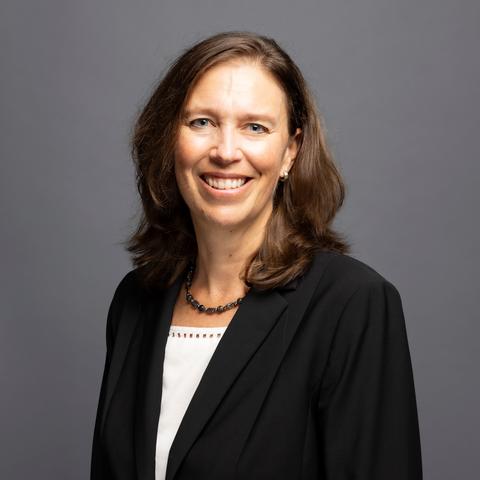 Jasinski posed for photo against a dark gray background wearing a black blazer and white blouse.