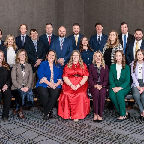 A group of adults posed for a formal photo in two rows inside a conference room.