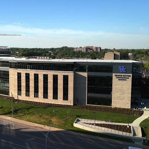 Aerial view of a modern University of Kentucky campus building beside a roadway, with surrounding green space and construction visible in the distance. 