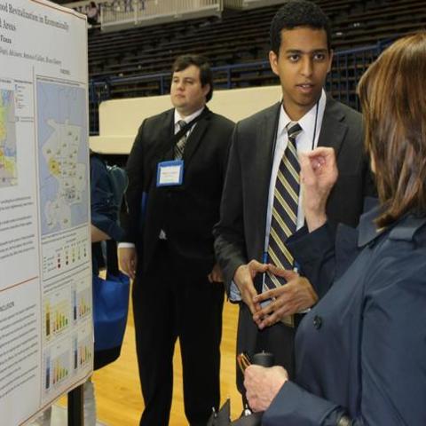 photo of male undergrad presenting research poster presentation to woman