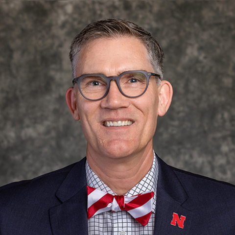 A portrait-style photo of Nick Pace wearing a navy blazer with a candy-cane-patterned bowtie and checkered dress shirt.