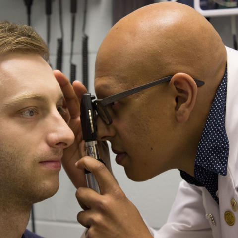 Paras Vora uses an ophthalmoscope to examine a male patient's eye