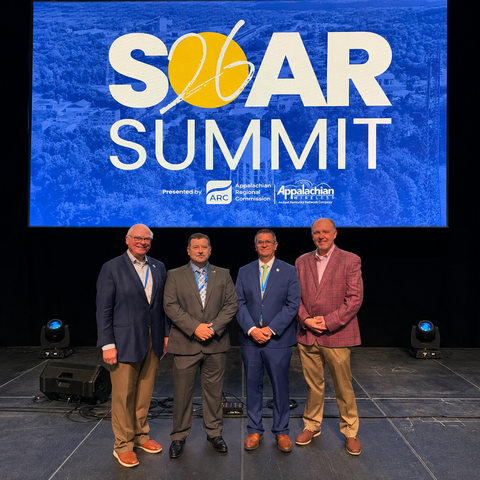 Four people stand together onstage beneath a SOAR Summit display.