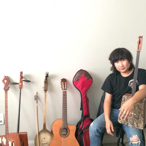 photo of Tamir Hargana seated by instruments and holding one