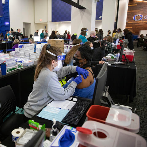 photo of several people in UK vaccination clinic including one woman getting a shot.