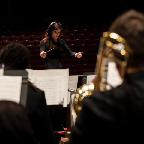 photo of Kaitlin Bove (in headphones) conducting UK Concert Band in 2018