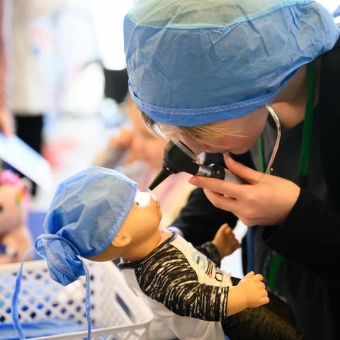 Child wearing surgical cap and examining doll 