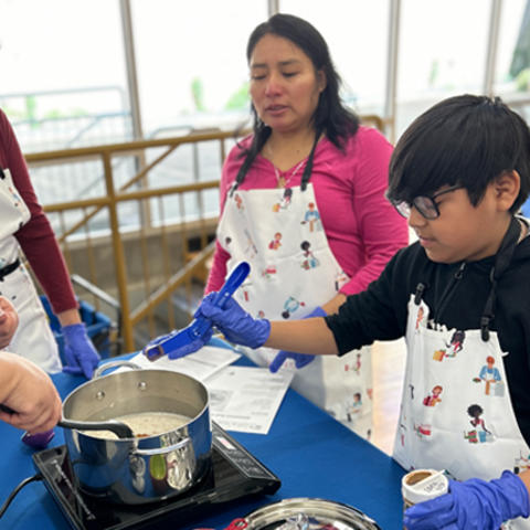 Image of a child getting a cooking lesson while his mother looks on