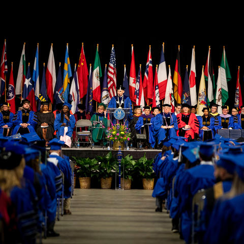 photo of December 2019 Commencement with flags on the platform where speakers and deans are sitting and President Capilouto at the podium