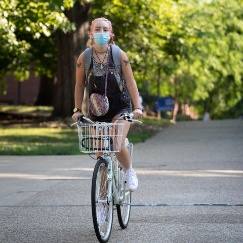 female student wearing mask bicycling on campus during covid pandemic