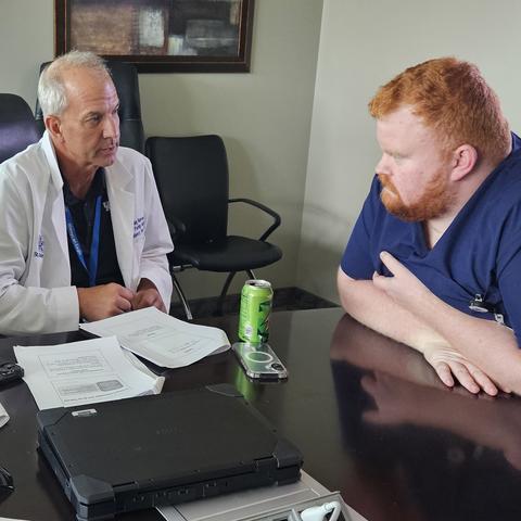 Doctor in white coat at center sitting at a table with a female resident on his left and male resident on right.