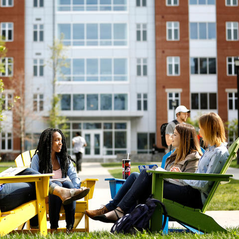 Photo of Students Sitting in Adirondack Chairs on Campus